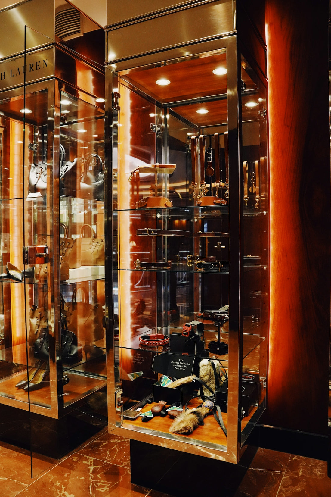 Leather handbags and pet accessories displayed in illuminated glass cabinets in a store